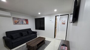 Un salon moderne avec un canapé noir, une table basse en bois et un téléviseur fixé au mur.