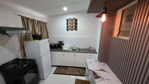 Une cuisine compacte équipée d’une cuisinière à gaz, d’un réfrigérateur et d’un four à micro-ondes. Un tapis à motifs recouvre le sol, et une table en bois surmontée d’un plan de travail en marbre s’y trouve.
