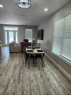 A dining area with a wooden table, chairs, a sofa, and a television mounted on the wall. - Black-Water River Retreat! to this Luxurious 3-bedroom 3.5 bath house (Milton)