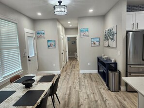 A modern kitchen with a stainless steel refrigerator, a dining area with a marble table, and a hallway with artwork.