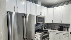 Une cuisine moderne équipée d’appareils électroménagers en acier inoxydable, de meubles blancs, d’un four à micro-ondes et d’une cuisinière à gaz.