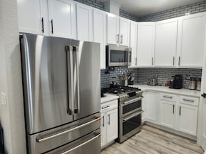 A modern kitchen with stainless steel appliances, white cabinets, a microwave, and a gas stove.