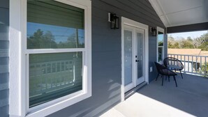 Une véranda avec une porte-fenêtre coulissante, un petit espace extérieur aménagé avec deux chaises, et une vue sur un quartier résidentiel.
