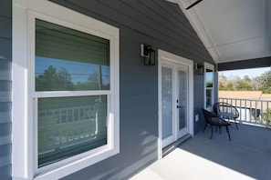 A covered porch with a sliding glass door, a small outdoor seating area with two chairs, and a view of a residential neighborhood.