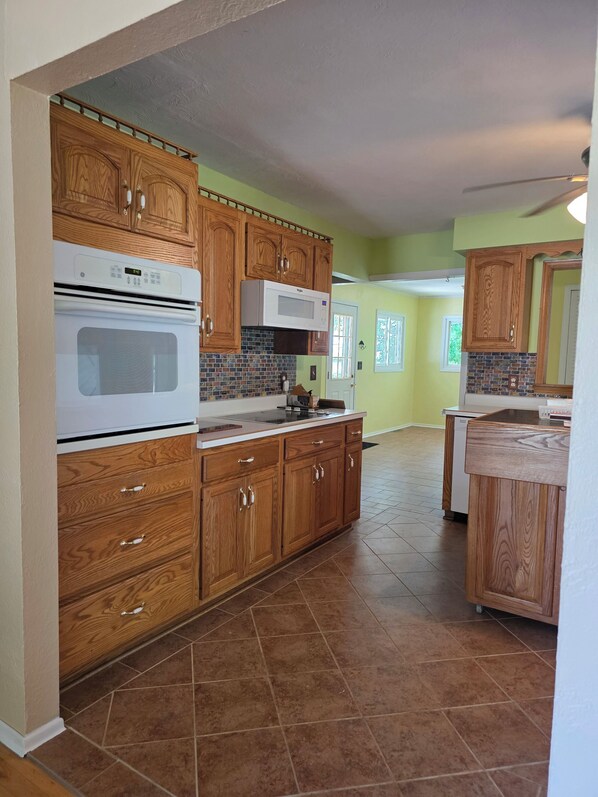 A kitchen with wooden cabinets, a microwave, an oven, and a tiled floor.
