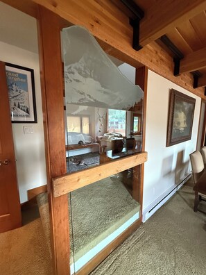 Ein Zimmer mit Holzboden, einem großen Fenster, einem gerahmten Bild an der Wand und einer Tür.