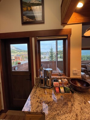 Une cuisine équipée d’une machine à café, d’un bol et d’une fenêtre donnant sur des immeubles et des arbres.