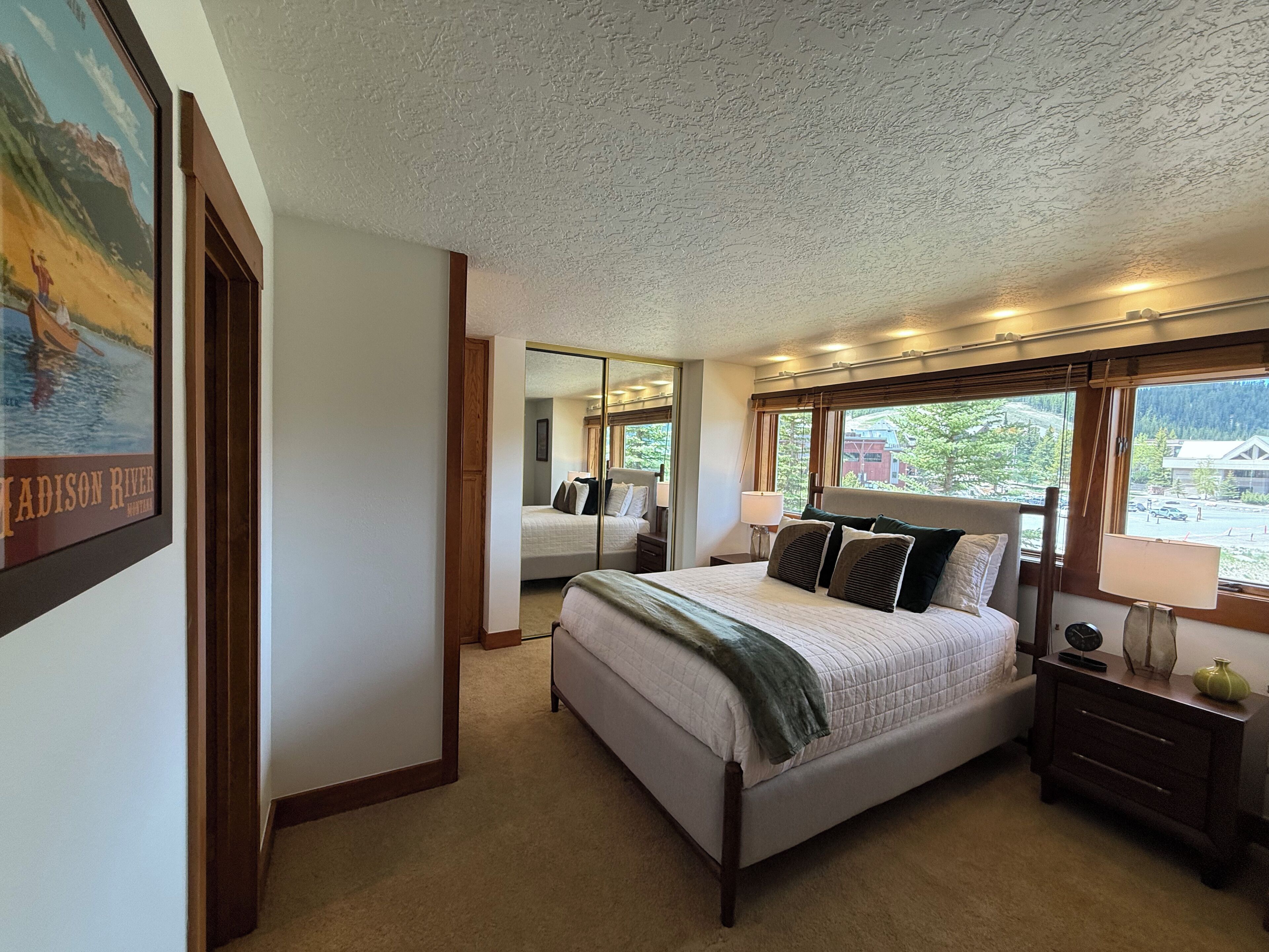 Une chambre à coucher avec un grand lit, une table de chevet, un miroir et une fenêtre donnant sur une montagne.