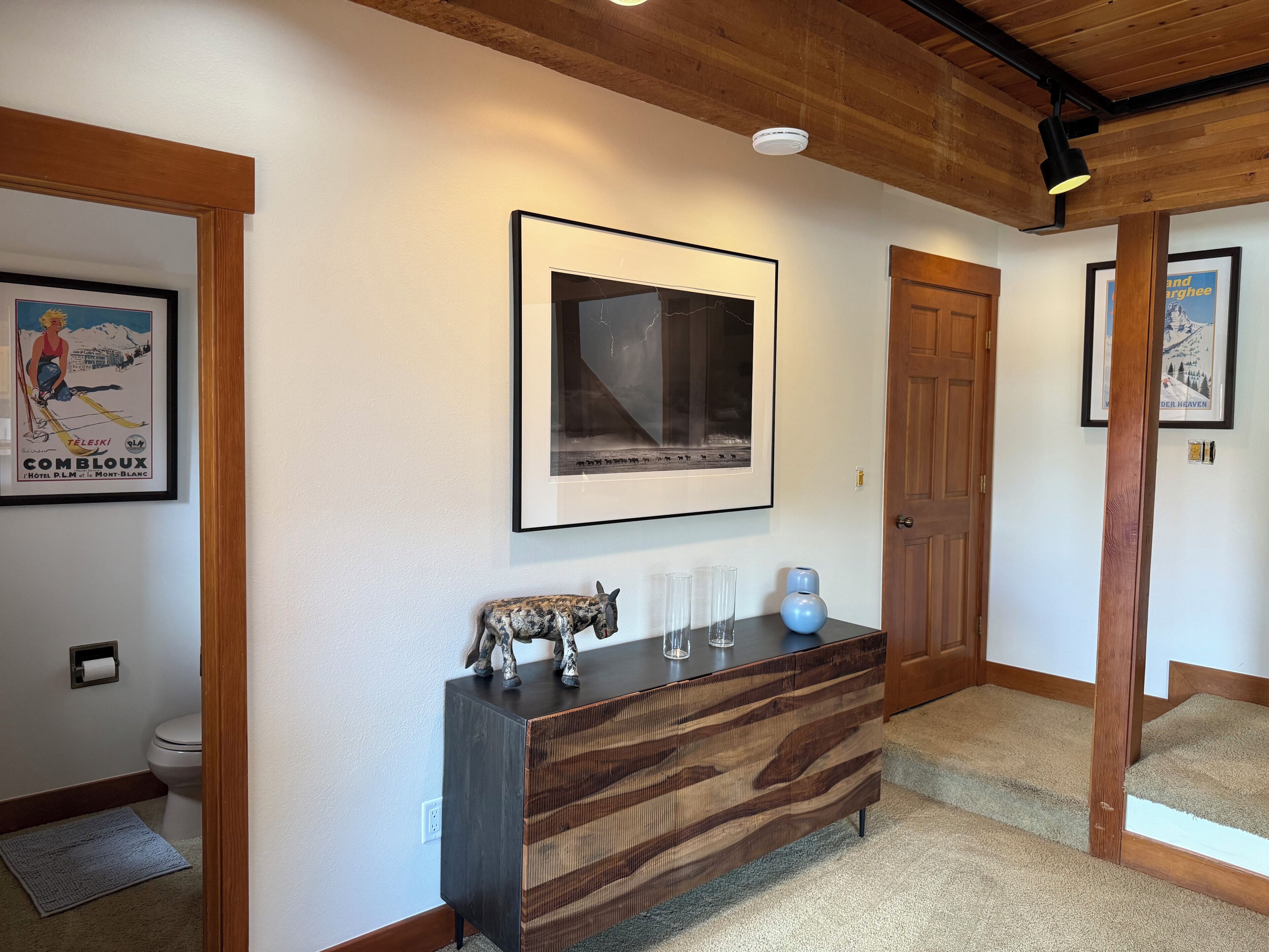 A hallway with a framed poster, a wooden cabinet with decorative items, and a door.