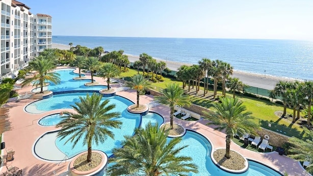 Um resort com uma grande área de piscina, palmeiras e vista para o oceano.