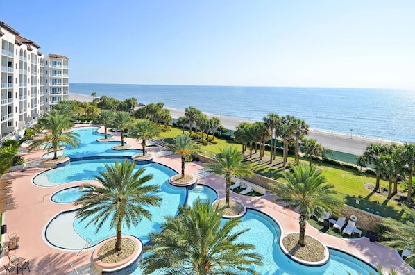 Un resort con un amplio área de piscina, palmeras y vista al océano.