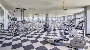 Uma academia com diversos equipamentos de exercícios, piso xadrez e amplas janelas.