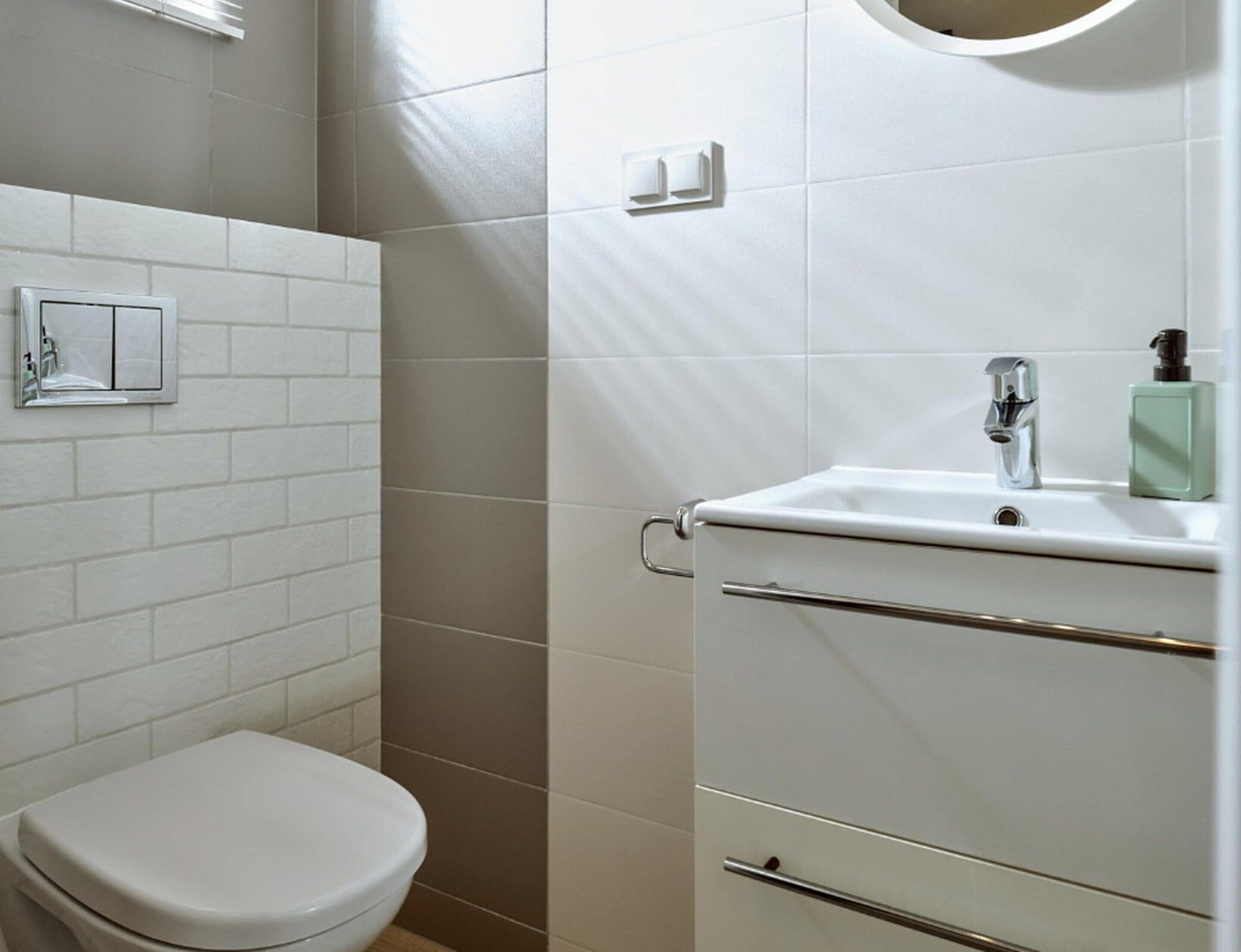 A bathroom with a toilet, a sink with a soap dispenser, and a towel rack.