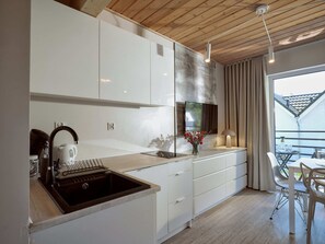 A modern kitchen with white cabinets, a black sink, and a dining area with a table and chairs. - Comfortable 2-room Apartments Close to the Beach (Mielno)