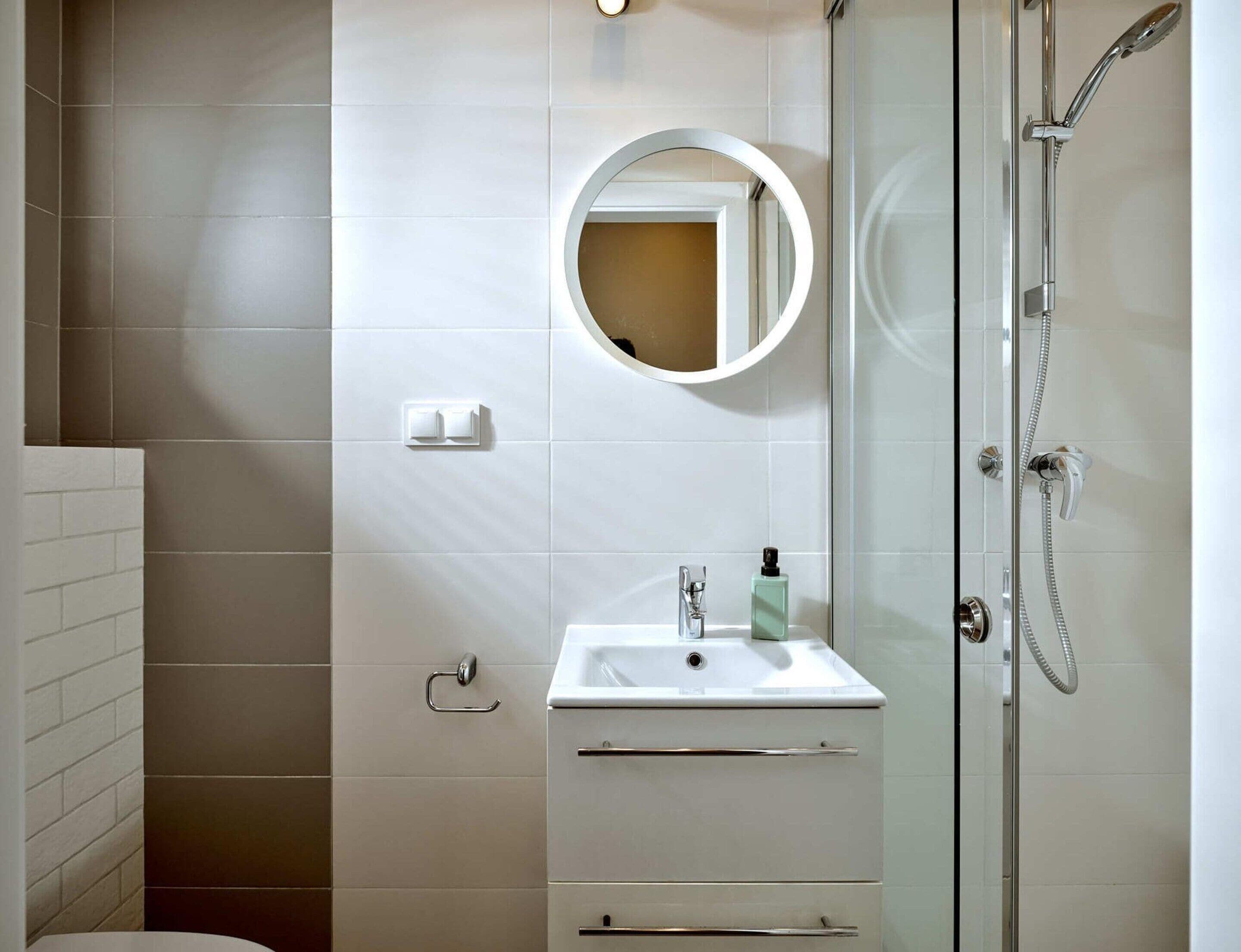Une salle de bain moderne avec une douche à parois de verre, un lavabo blanc avec un miroir rond et un porte-serviettes.