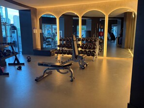 A gym with weightlifting equipment, a bench, and a mirror reflecting the interior. - Bright apartment in brilliant Dallas with AC and fitness room (Dallas)