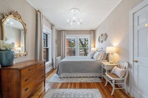 Een slaapkamer met een bed, een dressoir, een stoel, een nachtkastje, een kroonluchter en een grote spiegel.