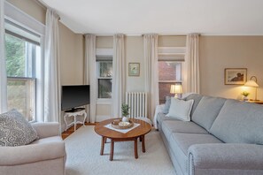 A living room with a sofa, a coffee table, a TV, and a lamp. - Heaton's Haven Suite B - Lovely apartment with king bed in a great location! (Baldwinsville)
