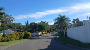 A residential street with houses, a white wall, and greenery.