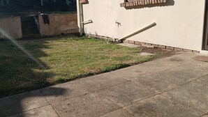 A building with a concrete patio, a grassy area, and a window with a traditional design.