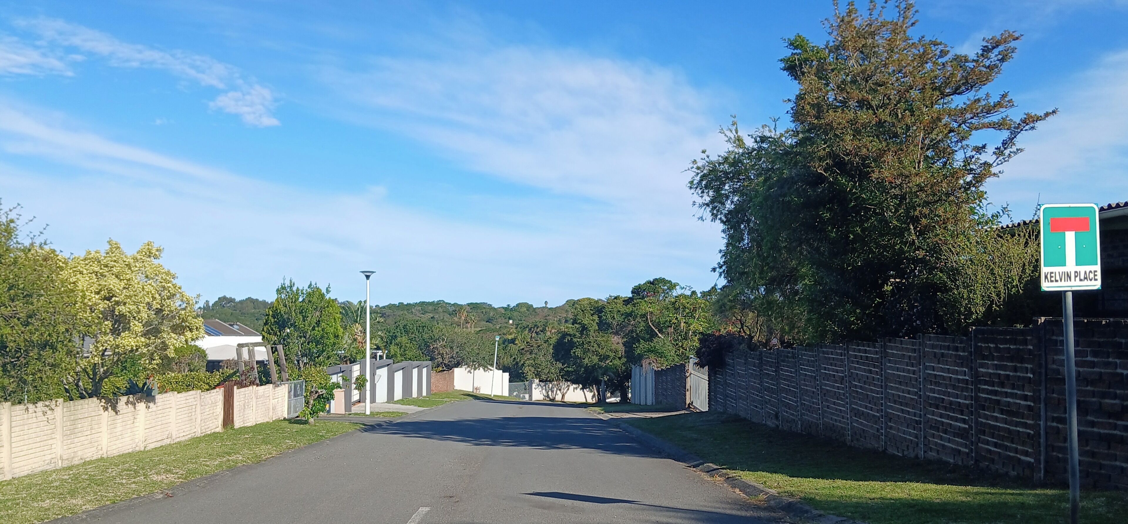 Een woonstraat met huizen, een kruispunt in de vorm van een T, en een bord waarop 'Kelvin Place' staat.