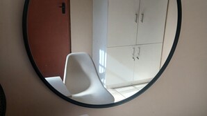 A room with a round mirror, a white table, two white chairs, and a white wardrobe.