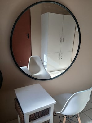 Een kamer met een ronde spiegel, een witte tafel, twee witte stoelen en een witte kledingkast.