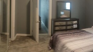 A bedroom with a bed, a dresser, a mirror, and a door leading to another room.