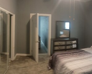 A bedroom with a bed, a dresser, a mirror, and a door leading to another room.