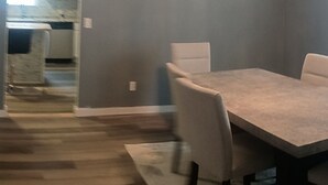 A dining area with a table and chairs, a chandelier, and a view of a kitchen and dining room through an open doorway.