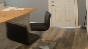 A room with a dining table, a black chair, a white door, and a broom leaning against the wall.