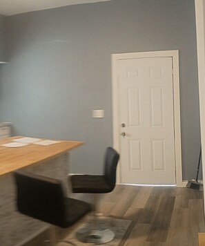 Ein Zimmer mit einem Esstisch, einem schwarzen Stuhl, einer weißen Tür und einem an die Wand gelehnten Besen.