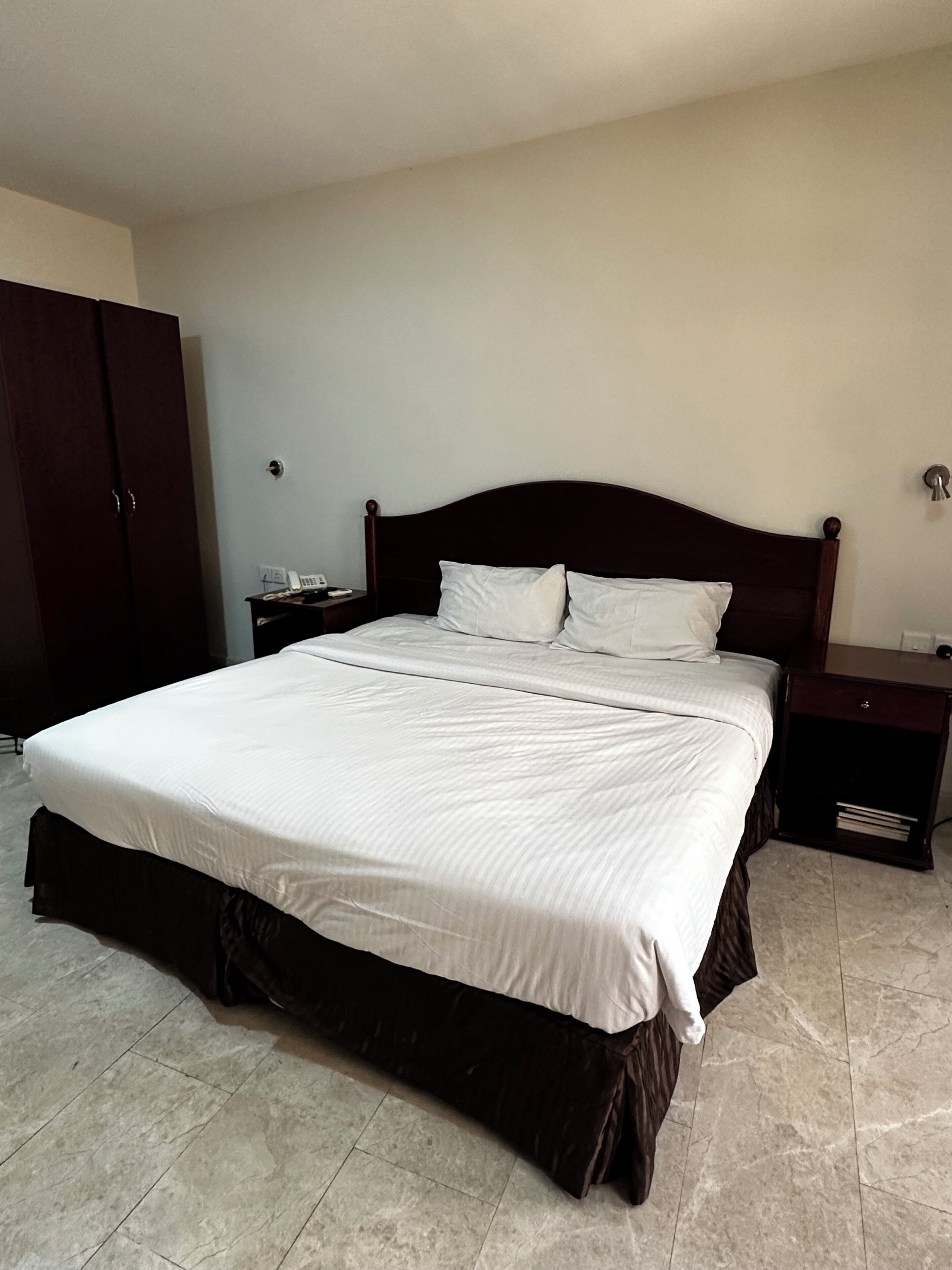 A standard hotel room with a large bed, a wardrobe, a bedside table, and a nightstand.