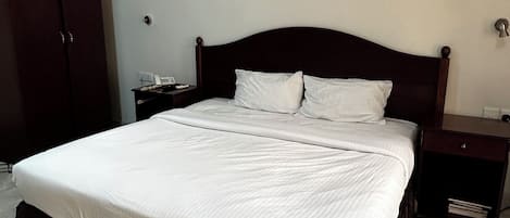 A standard hotel room with a large bed, a wardrobe, a bedside table, and a nightstand.
