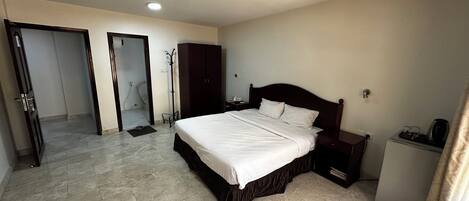Ein Hotelzimmer mit einem großen Bett, einem Schrank, einem Schreibtisch mit Stuhl, einer kleinen Ablage und einem sichtbaren Badezimmer hinter einer offenen Tür.