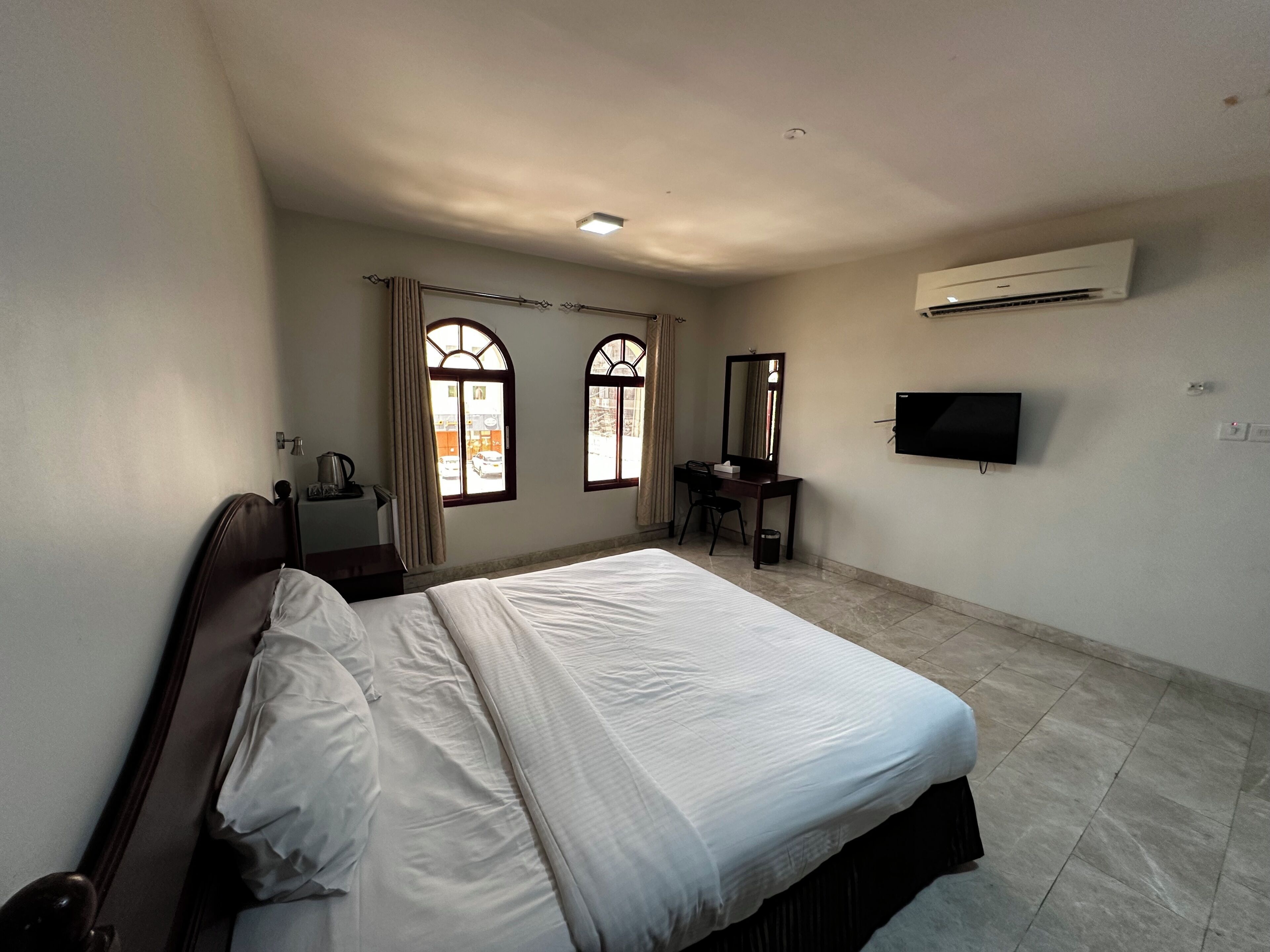 A hotel room with a bed, a desk, a chair, a television, and an air conditioning unit.