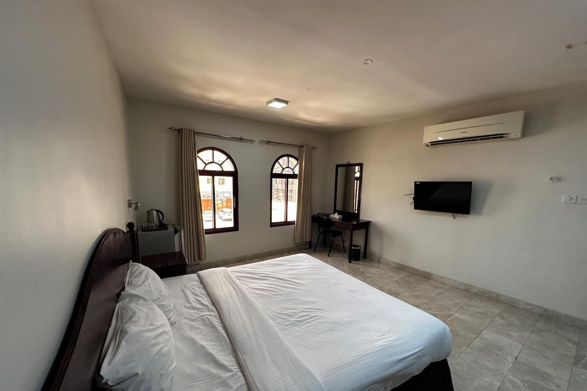 Habitación de hotel con cama, escritorio, silla, televisor y aire acondicionado.