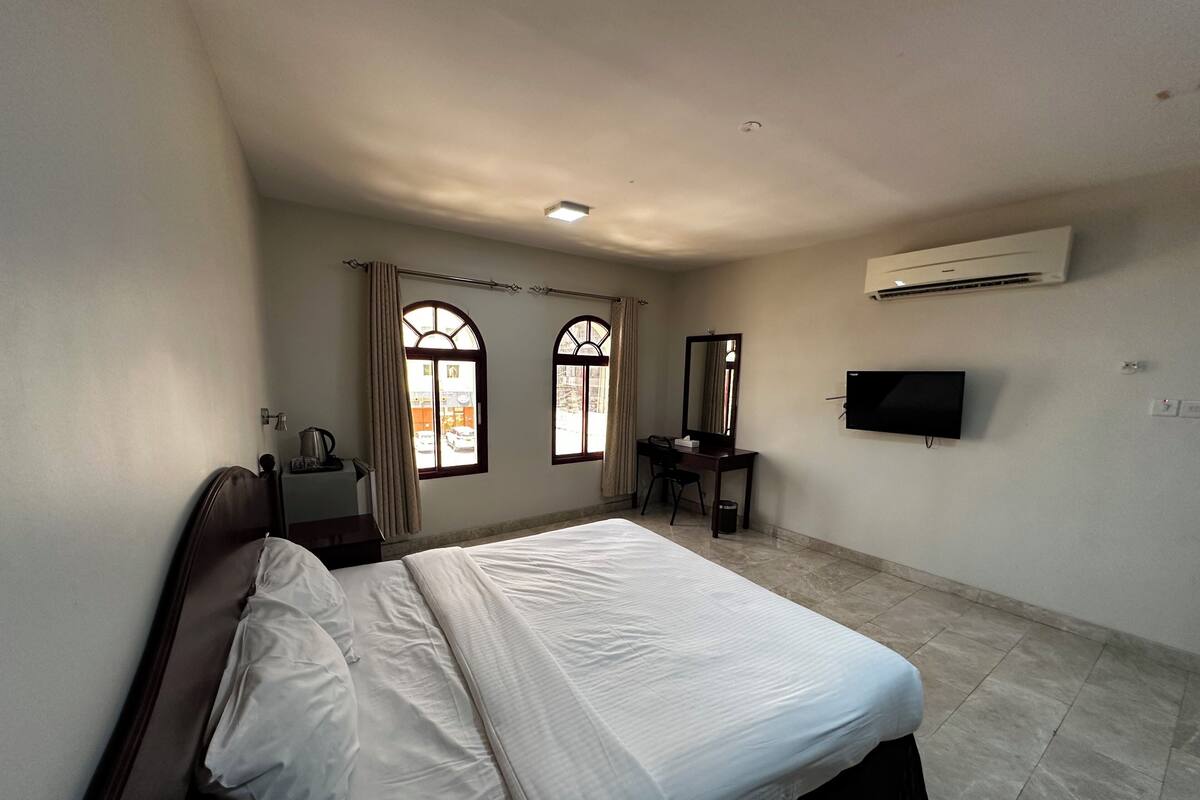 A hotel room with a bed, a desk, a chair, a television, and an air conditioning unit.