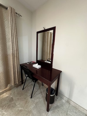 A small, dark wooden desk with a mirror, a black chair, a tissue box, and a trash can. - Alreef Hotel Suites (Muscat)