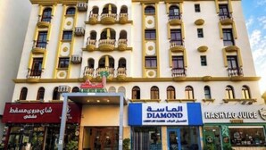 Un hotel de varios pisos con balcones, un letrero que dice 'Diamond Juice' y un comercio con letreros en árabe.