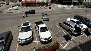 Un estacionamiento con varios autos, un edificio de varios pisos y una estructura más pequeña adyacente.