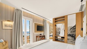 A hotel room with a bed, a TV, a desk, and a view of the sea.