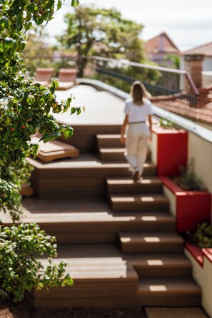 Uma pessoa caminhando por uma escadaria com corrimão de um lado e um vaso vermelho do outro.