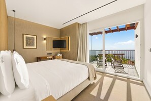 Quarto de hotel com uma cama grande, televisão de tela plana, uma pequena mesa de trabalho e varanda com vista.