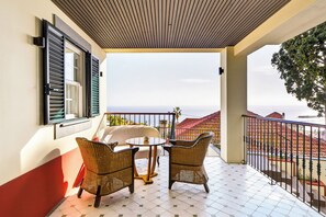 Ein Balkon mit Korbmöbeln, Fliesenboden und Blick auf Gebäude und das Meer.