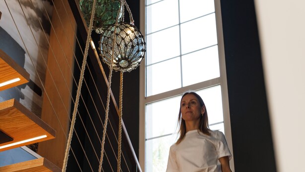A staircase with wooden steps and metal railings, a person wearing white pants and a white shirt, and a large window with natural light.