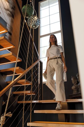 A staircase with wooden steps and metal railings, a person wearing white pants and a white shirt, and a large window with natural light. - Cais 68 Luxury Boutique Villa - Adults Only - 24h Concierge (Funchal)