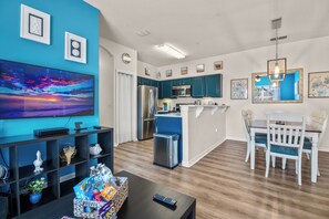 A modern kitchen with blue cabinets, a stainless steel refrigerator, and a dining area with white chairs. - Cozy 2-bedroom Condo with AC near Disney (Kissimmee)