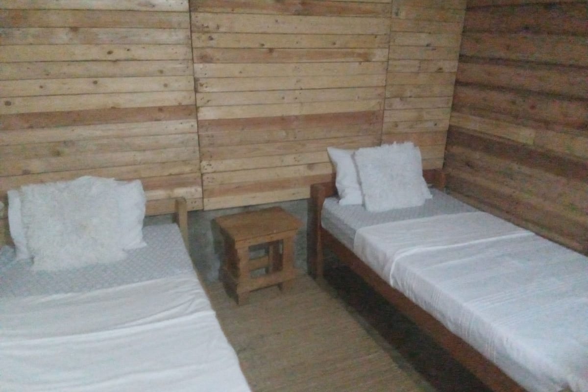 Una habitación con dos camas de madera, un taburete pequeño de madera y un panel de madera en la pared.