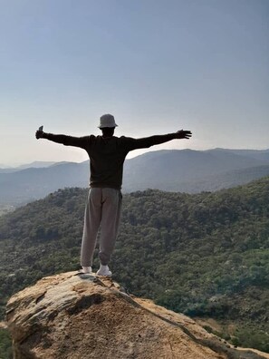 A person standing on a rock with arms outstretched, overlooking a mountainous landscape. - Tfutjana Mount resort and restaurant (Kholwane)
